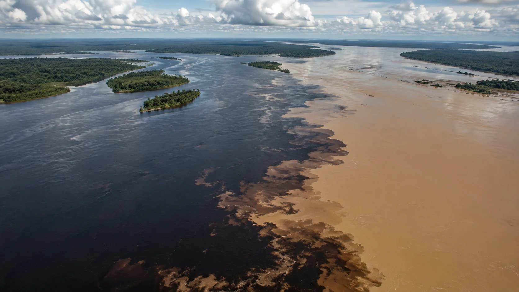 Dunkles Wasser des Rio Negro und helles Wasser des Solimões treffen in einer weiten amazonischen Flusslandschaft aufeinander.